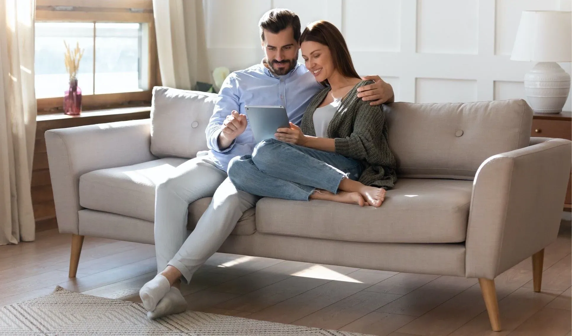 Image of a couple, sitting on a couch, looking at a mobile device.